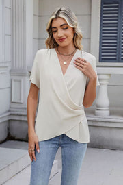 Cream draped front short sleeve blouse with a V-neckline and asymmetrical hem.