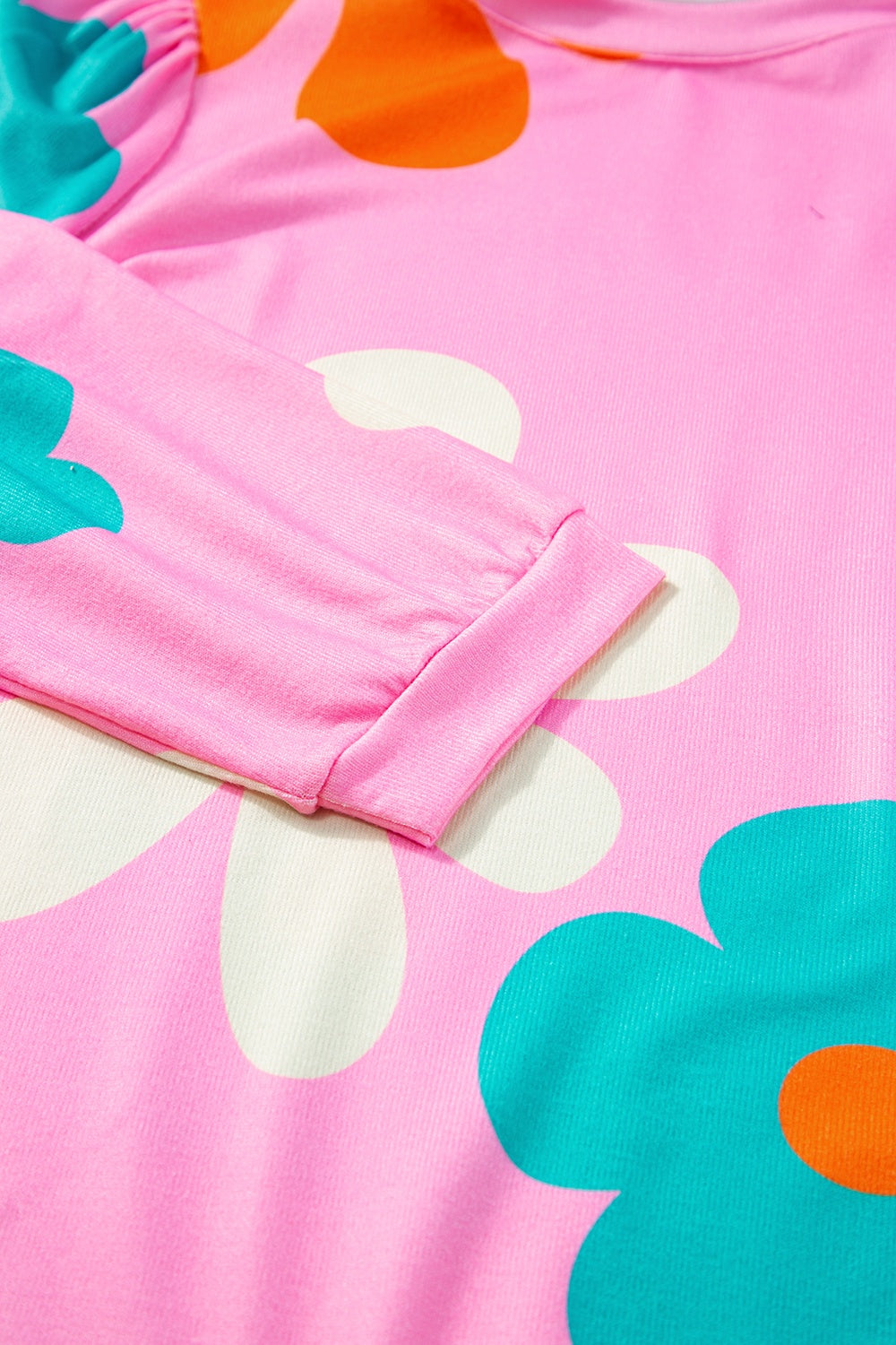 Pink t-shirt with a bold floral print in teal, orange, and white.
