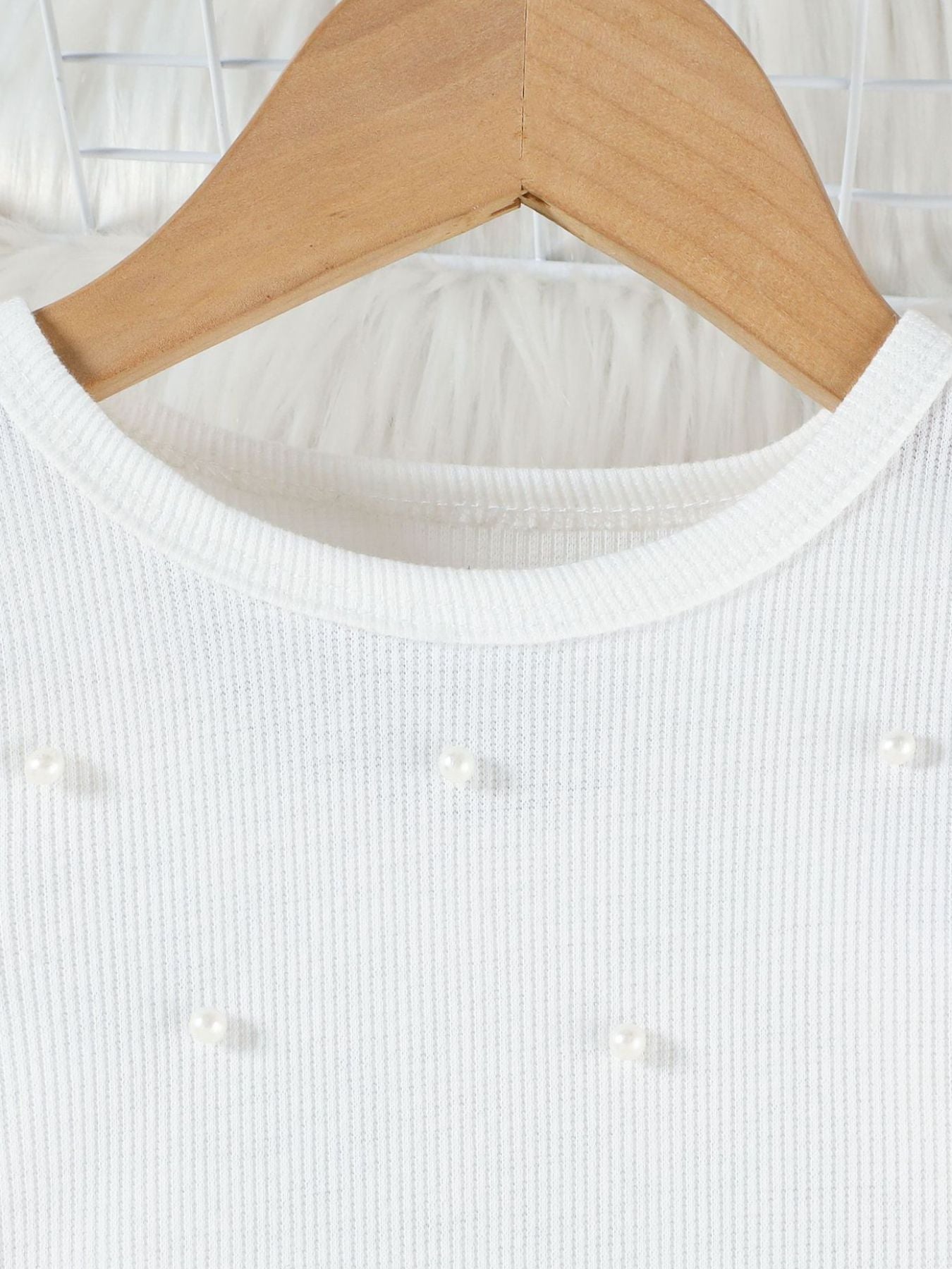White baby top with pearl embellishments and ribbed texture.