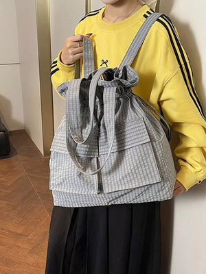 Grey plaid drawstring backpack with front pockets and adjustable straps.