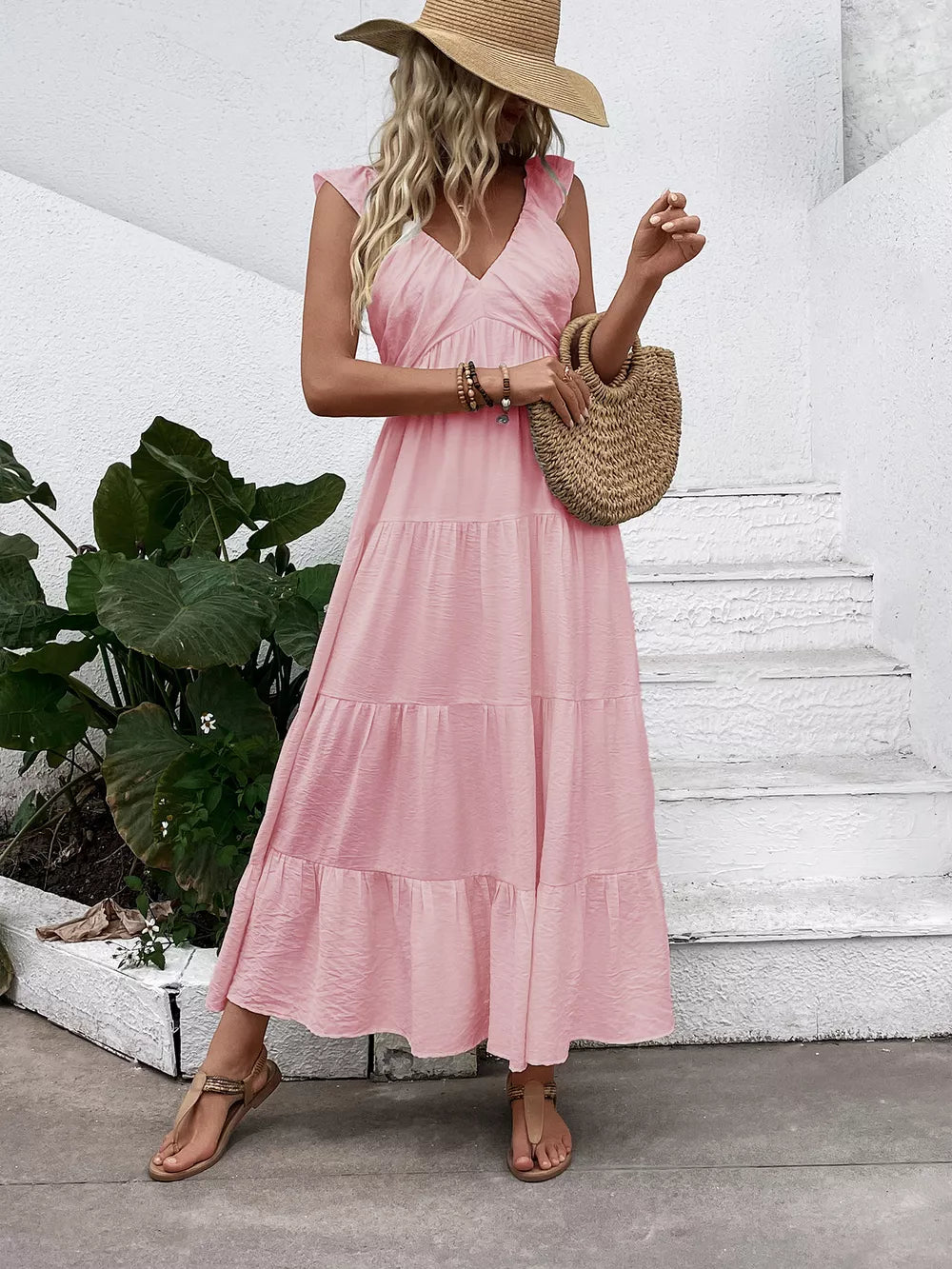 Blush pink tiered maxi dress with flutter sleeves and V-neck, styled with a straw hat and bag.