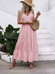 Blush pink tiered maxi dress with flutter sleeves and V-neck, styled with a straw hat and bag.