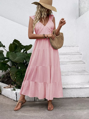 Blush pink tiered maxi dress with flutter sleeves and V-neck, styled with a straw hat and bag.