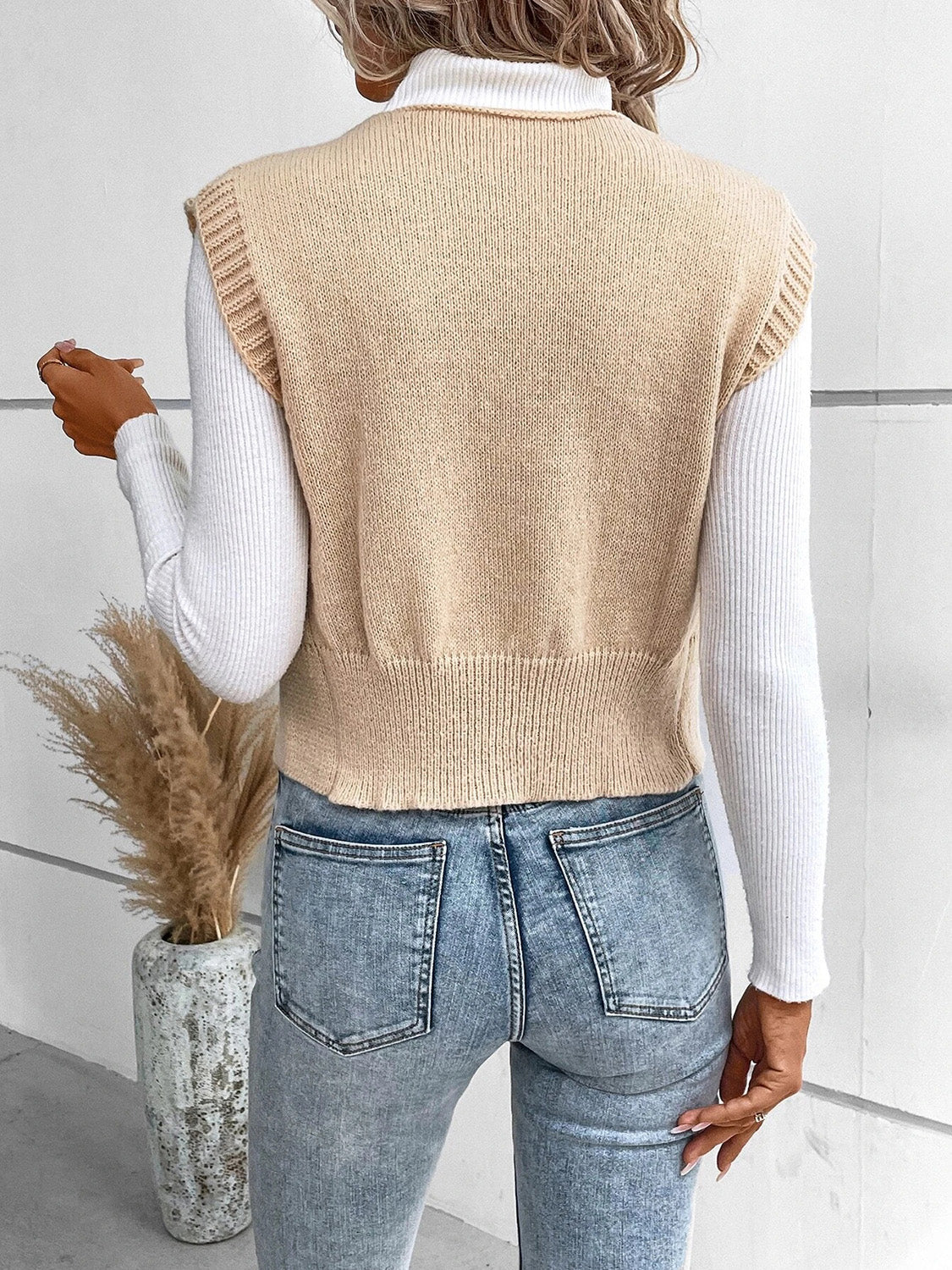 Tan acrylic knit vest with ribbed trim and hem, worn over a white turtleneck.
