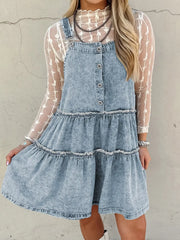 Tiered denim overall dress in light blue with button front and frayed hem tiers.