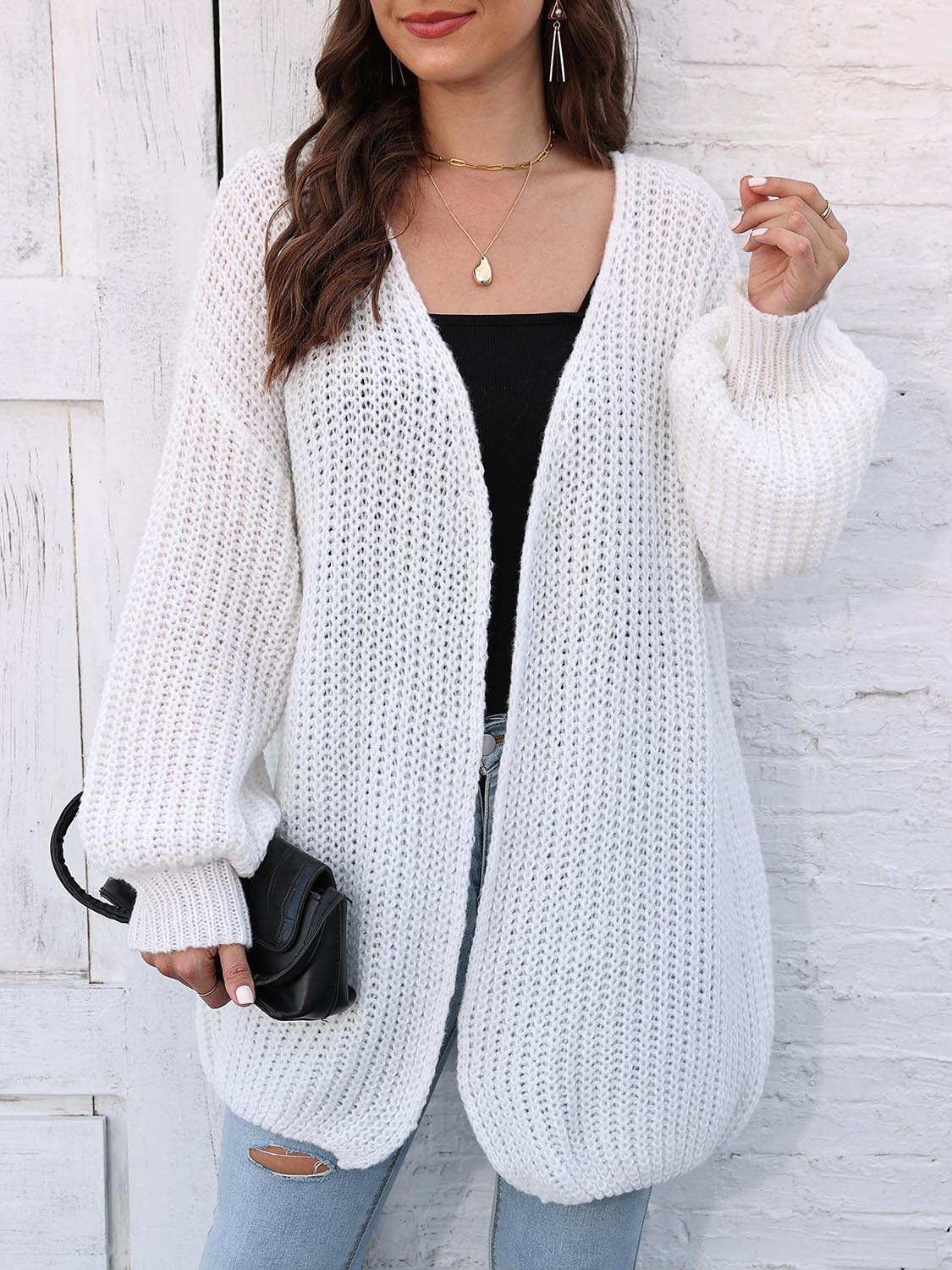 White open knit cardigan with balloon sleeves and ribbed cuffs, styled with a black top.