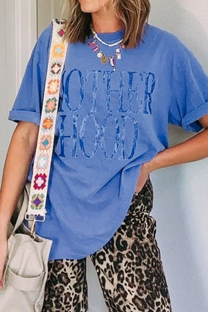 Blue oversized graphic tee with "MOTHERHOOD" text, rolled sleeves, and a crew neck.