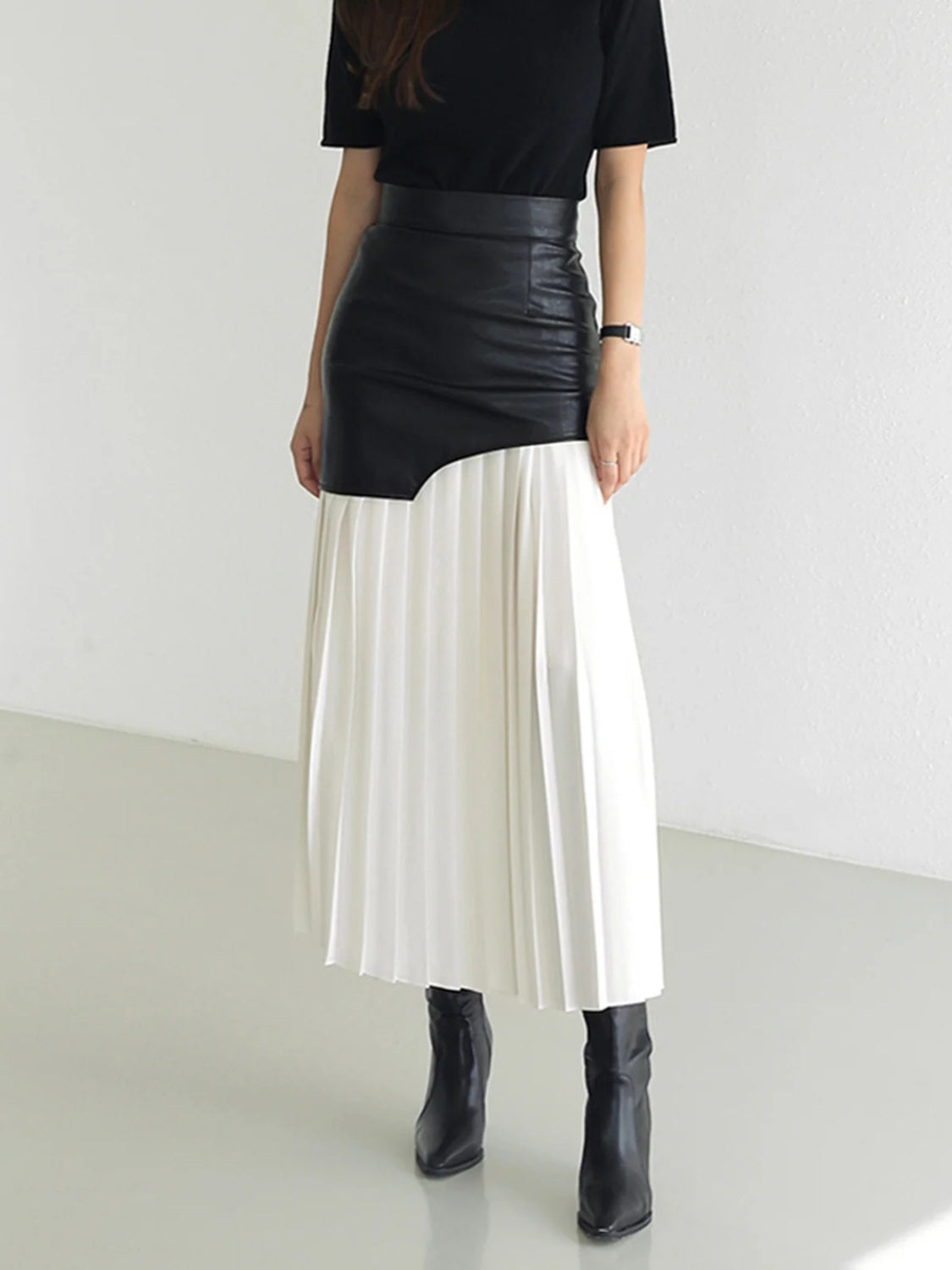 Asymmetric black leather top midi skirt with white pleated panel and black boots.