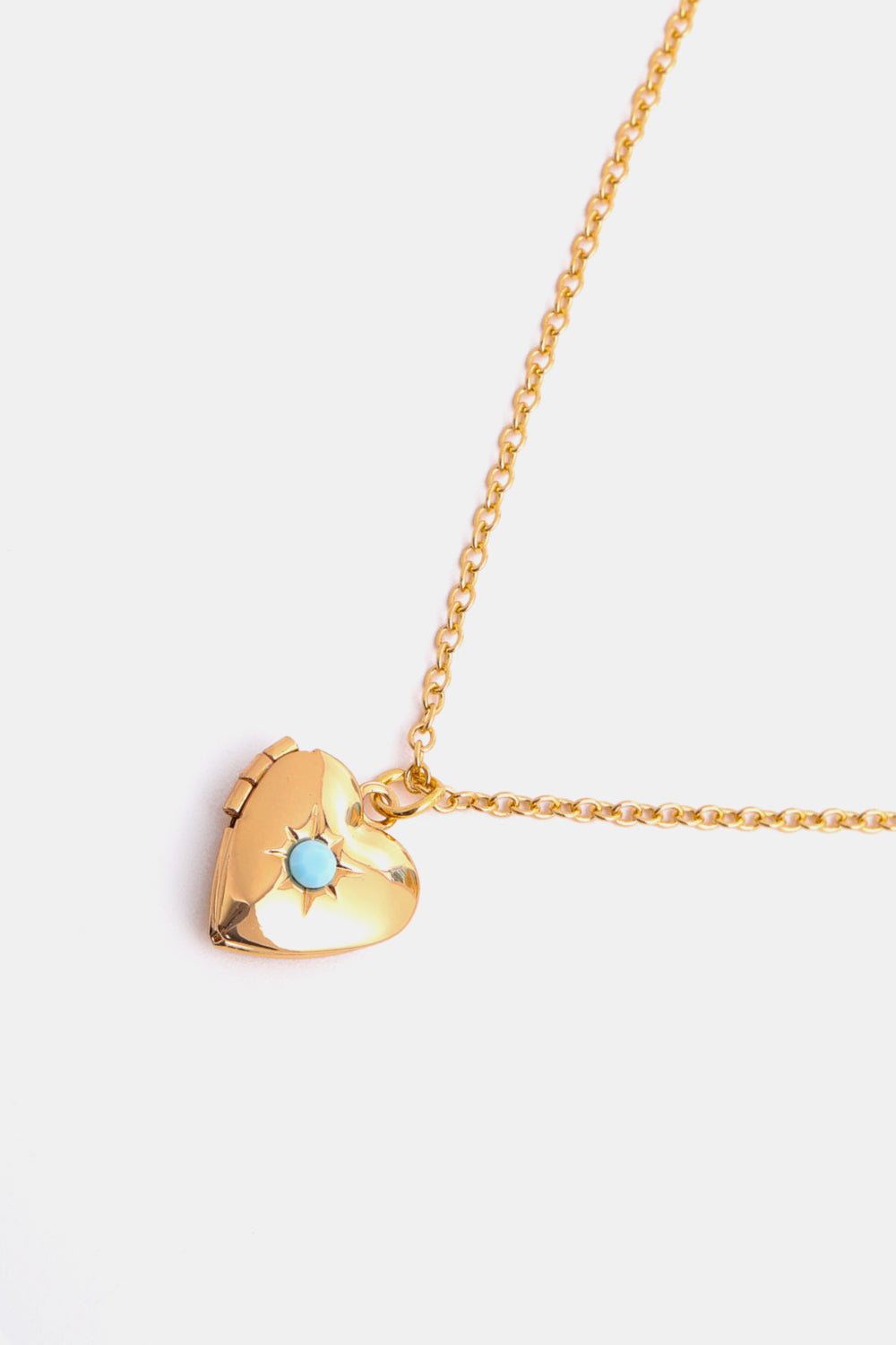 Gold heart locket necklace with turquoise accent and starburst engraving on a delicate chain.