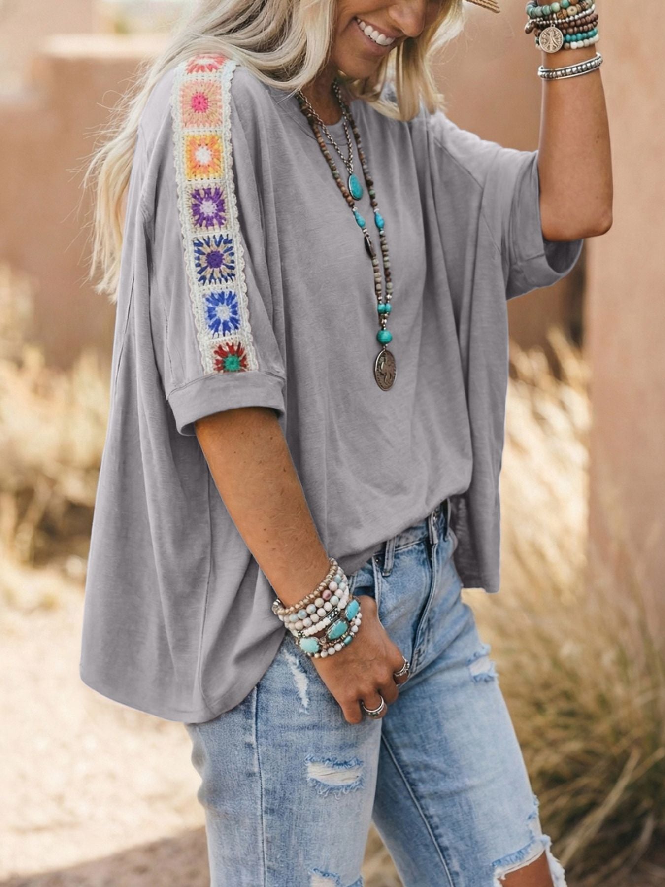 Grey t-shirt with colorful crochet detail on the sleeves and a loose fit.