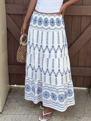 Bohemian white maxi skirt with blue floral embroidery and tiered ruffles.