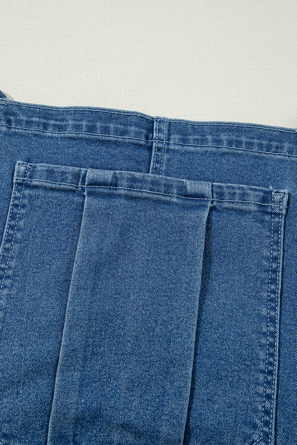 Medium wash denim wide-leg overalls with buttoned front and adjustable straps.