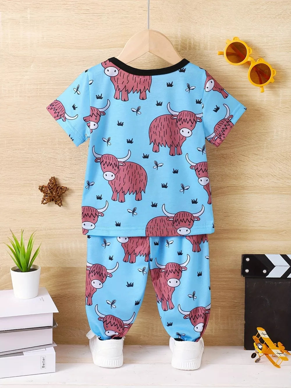 Baby pajama set with blue highland cow print, short sleeves, and elastic waist pants.
