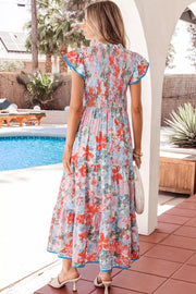 Vibrant floral maxi dress with smocked bodice, flutter sleeves, tiered skirt, and blue trim.