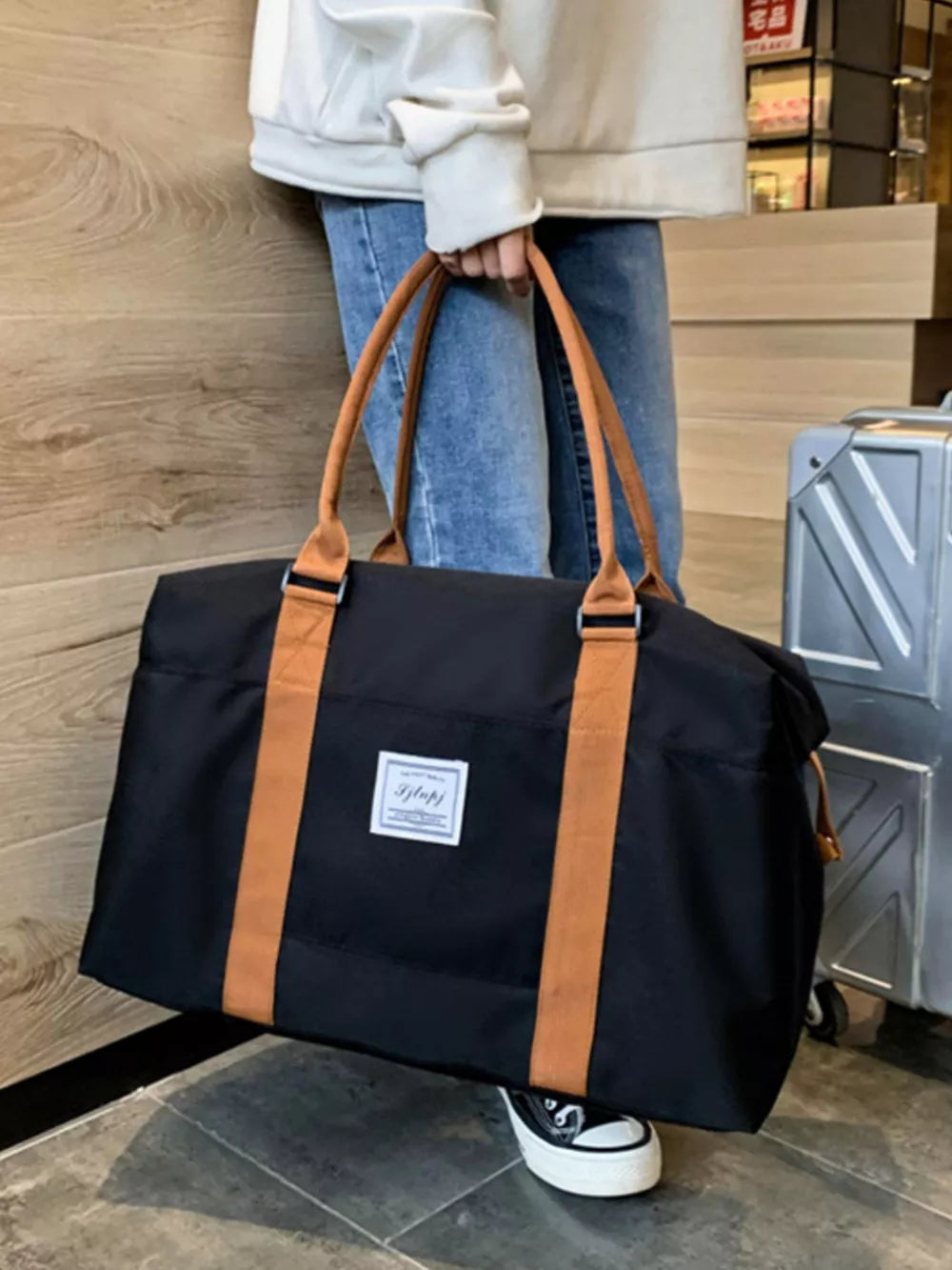 Large black Oxford cloth travel bag with tan contrast straps and a white label.