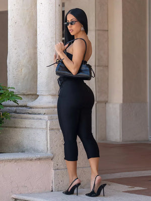 Black strapless jumpsuit with cinched waist and cropped pants, worn with heels.