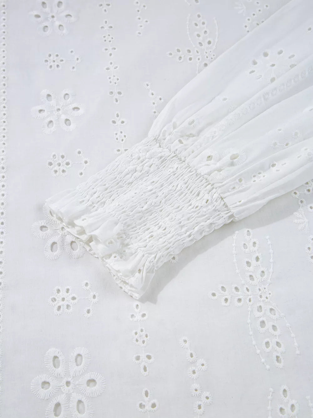White cotton blouse with eyelet embroidery and smocked cuff detail.