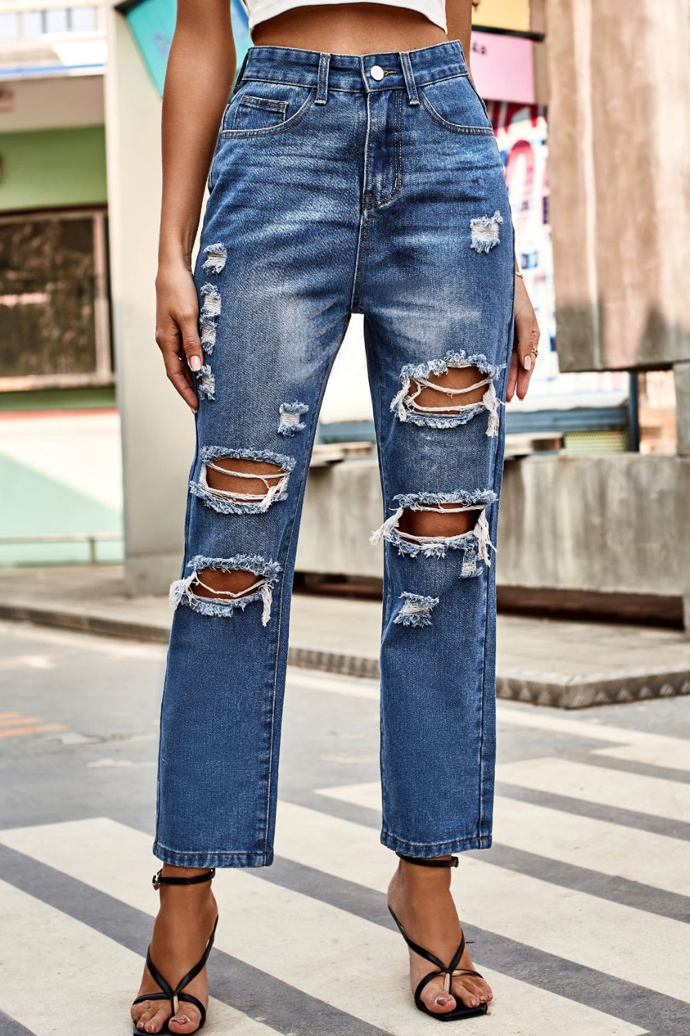 Distressed straight leg denim jeans in medium wash with ripped detailing.