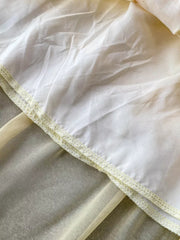 Floral ruffled two-piece ensemble detail showing sheer yellow fabric layered under white with decorative stitching.