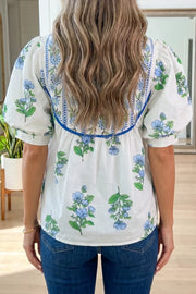 White polyester shirt with blue floral print, puff sleeves, and embroidered neckline detail.