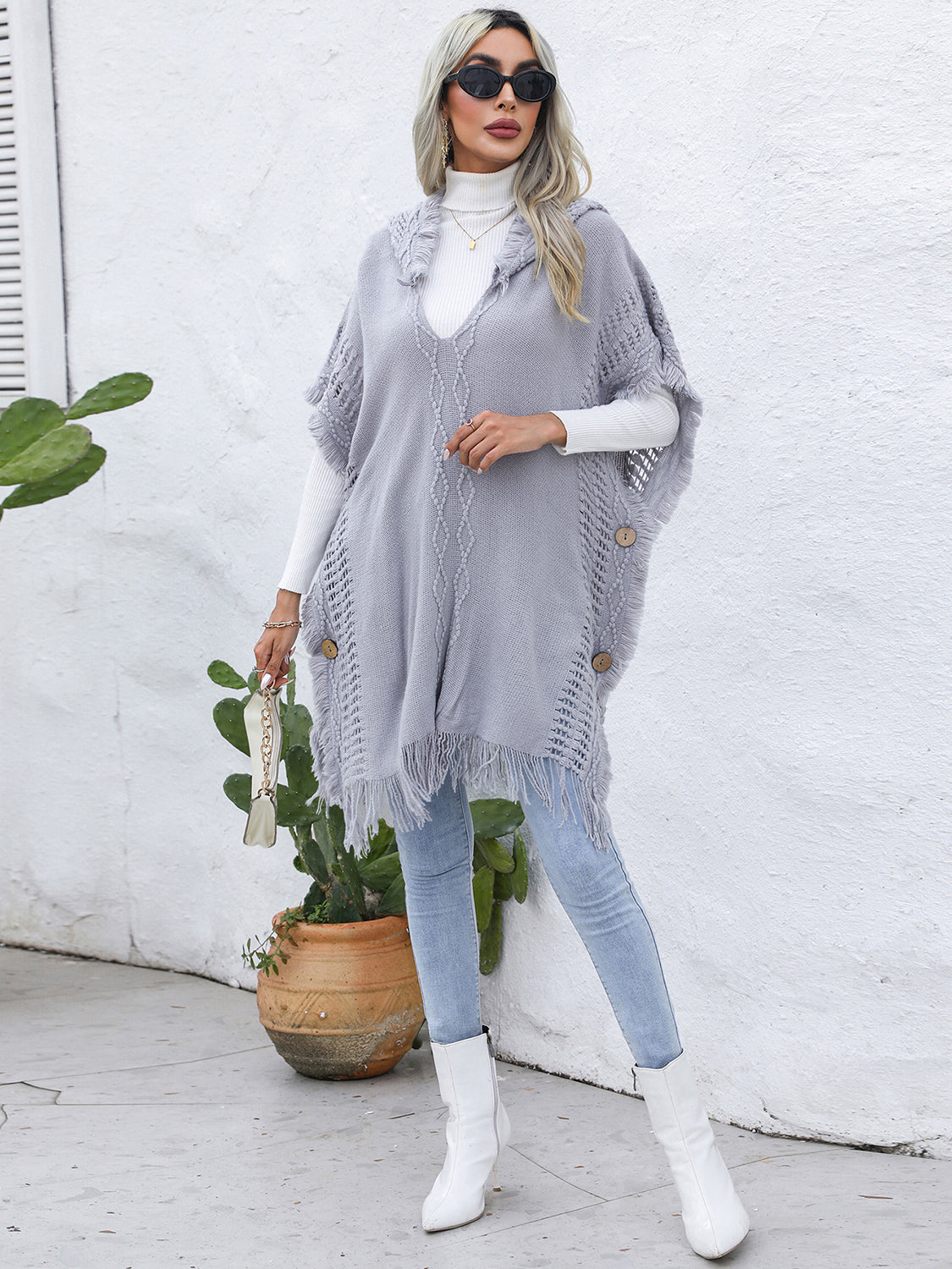 Light gray knit poncho with fringe, V-neck, wooden buttons, and diamond pattern detail.