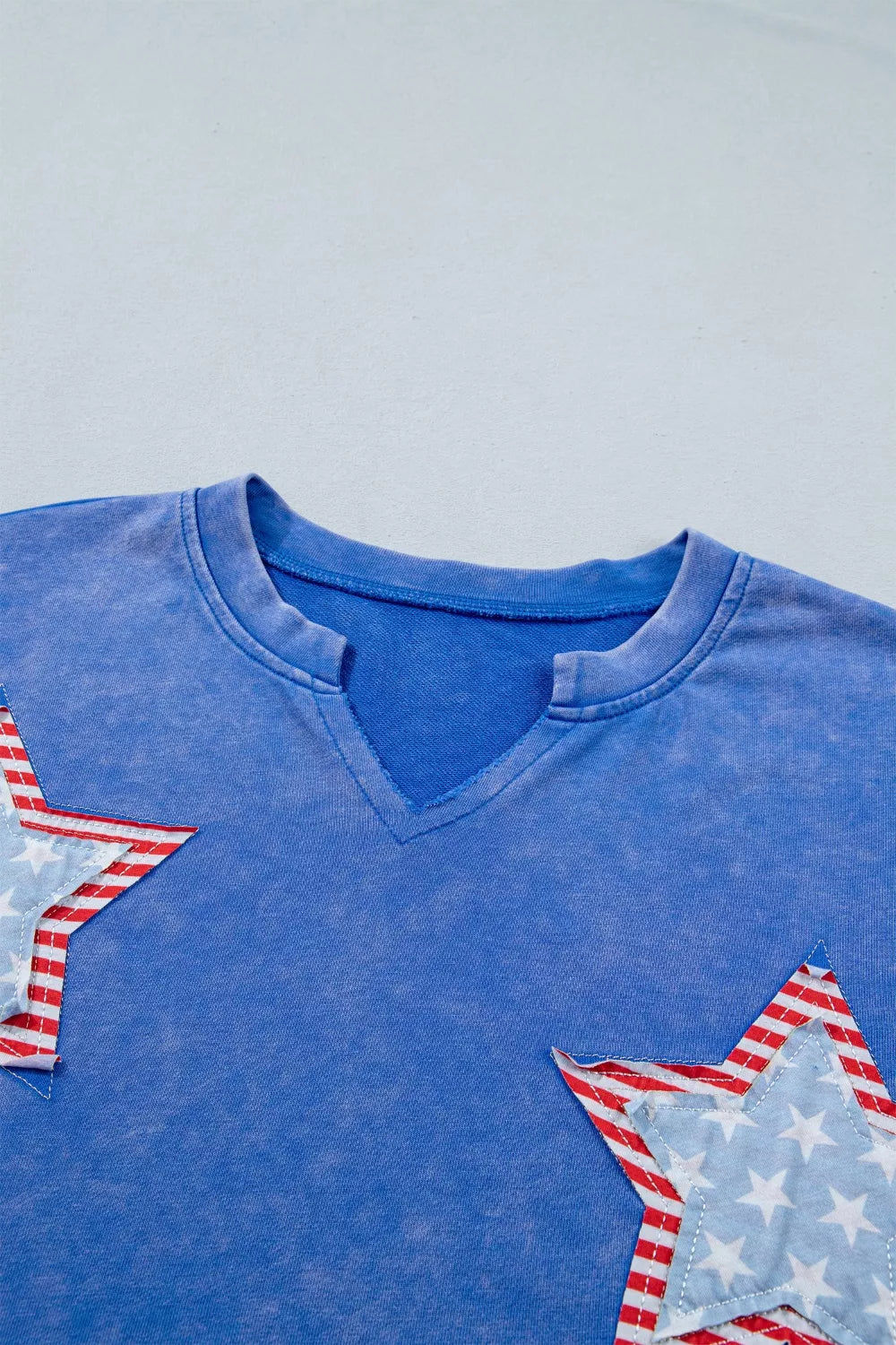 Blue cotton t-shirt with notched neck and patriotic star appliqués.