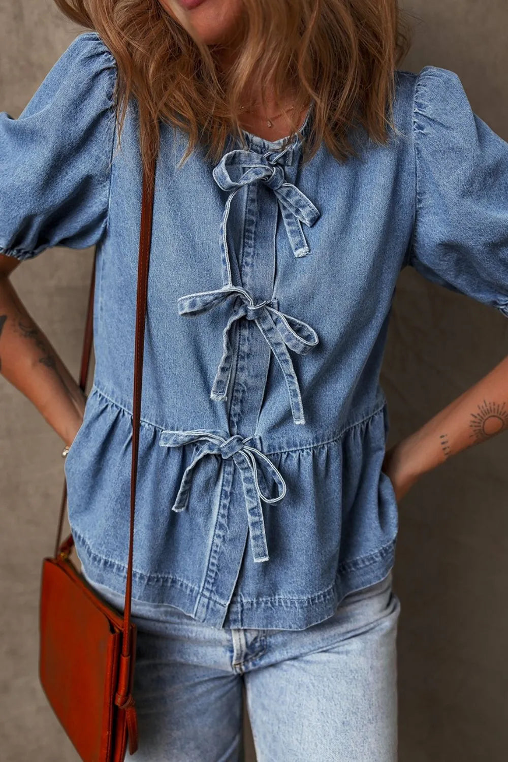 Denim peplum blouse with puff sleeves and multiple bow ties down the front.