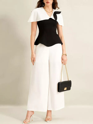 Black peplum top with white cape collar and bow detail, paired with white wide-leg pants.