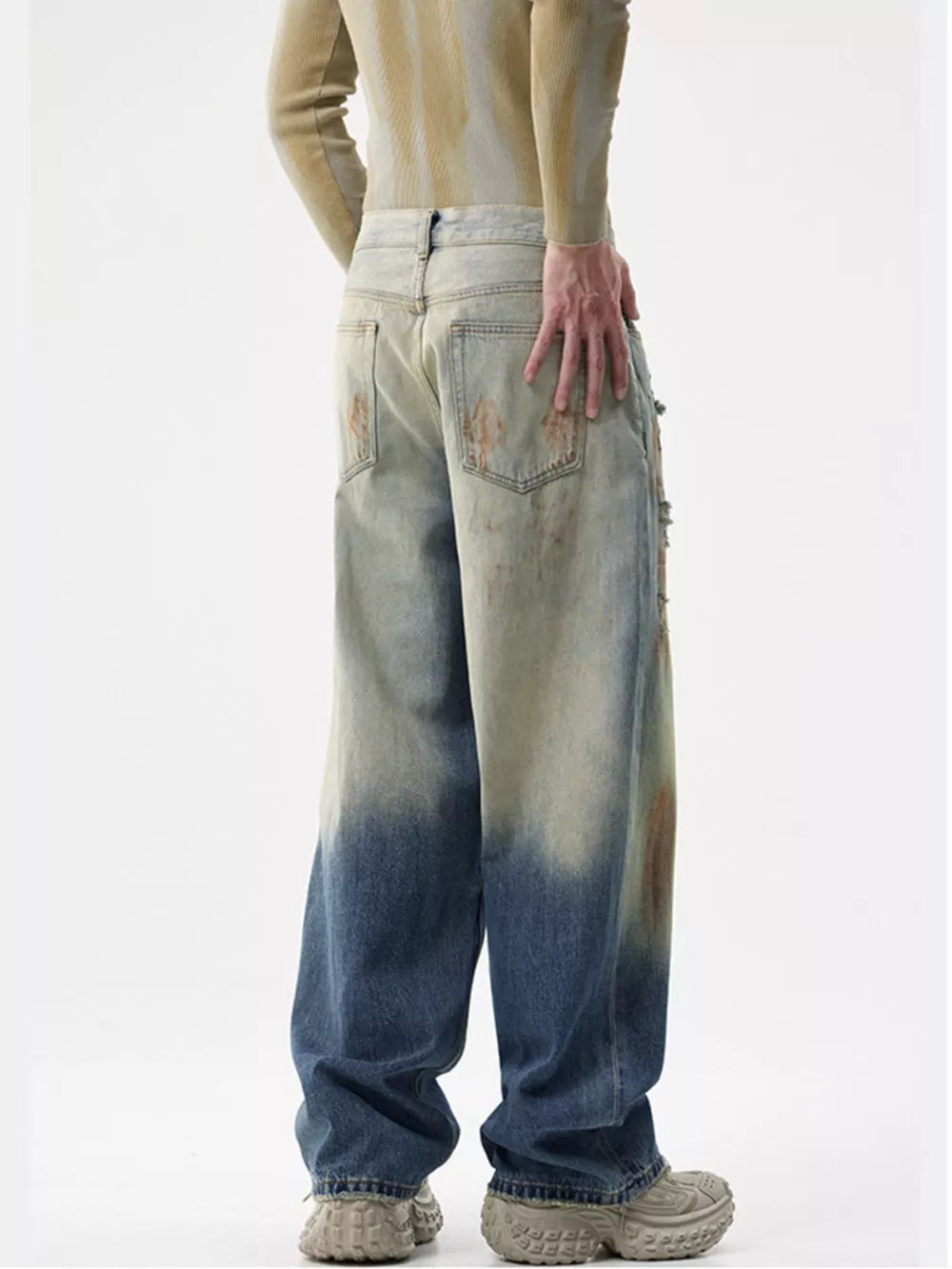 Men's distressed wide-leg jeans with a faded blue and tan ombre wash and brown stain details.