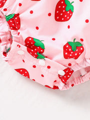 Baby one-piece in blush pink with strawberry print, polka dots, and snap closures.
