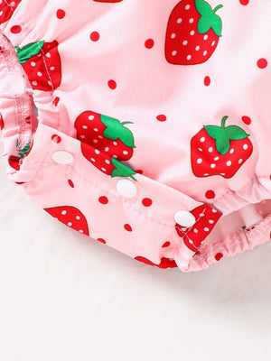 Baby one-piece in blush pink with strawberry print, polka dots, and snap closures.