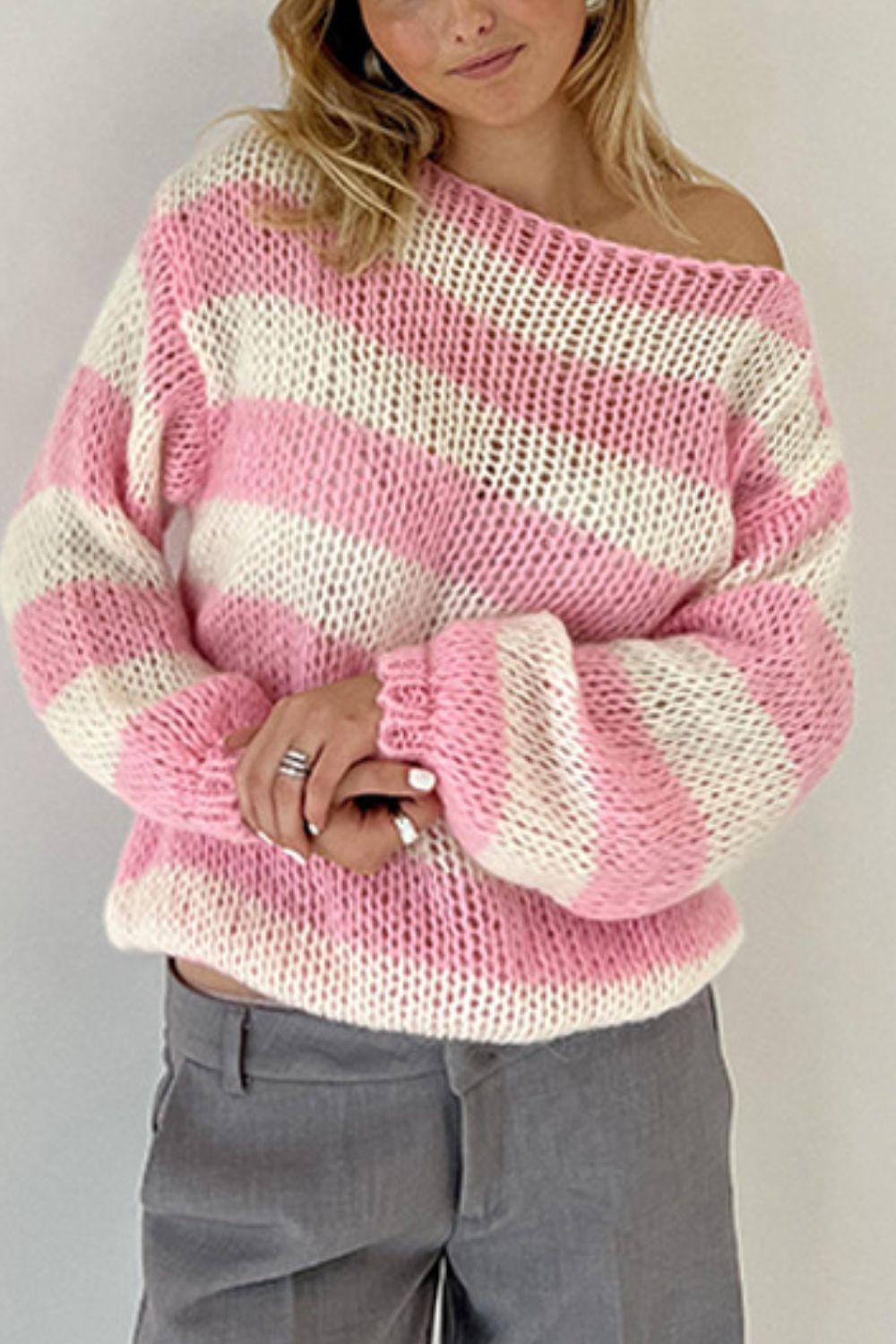 Off-shoulder striped knit sweater with voluminous sleeves in blush pink and white.
