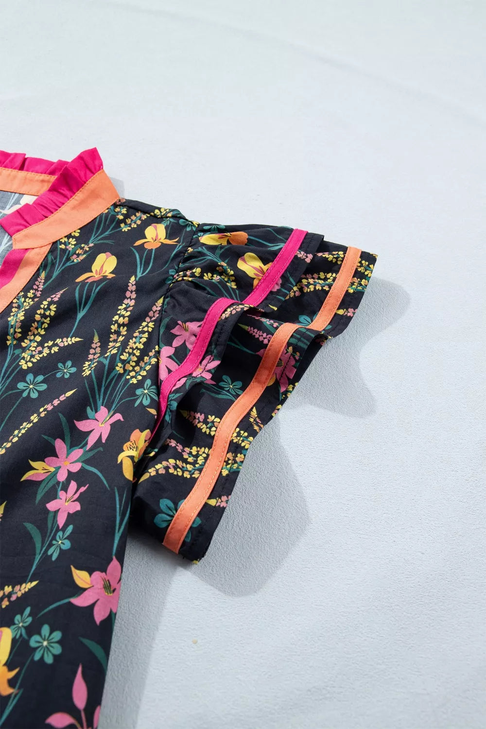 Black cotton blouse with vibrant floral print, contrast trim, and ruffled neckline.