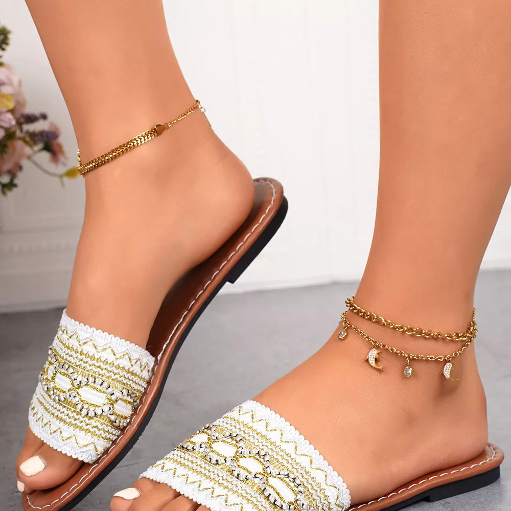 White embroidered artisan open-toe sandals with gold accents and chain anklets.