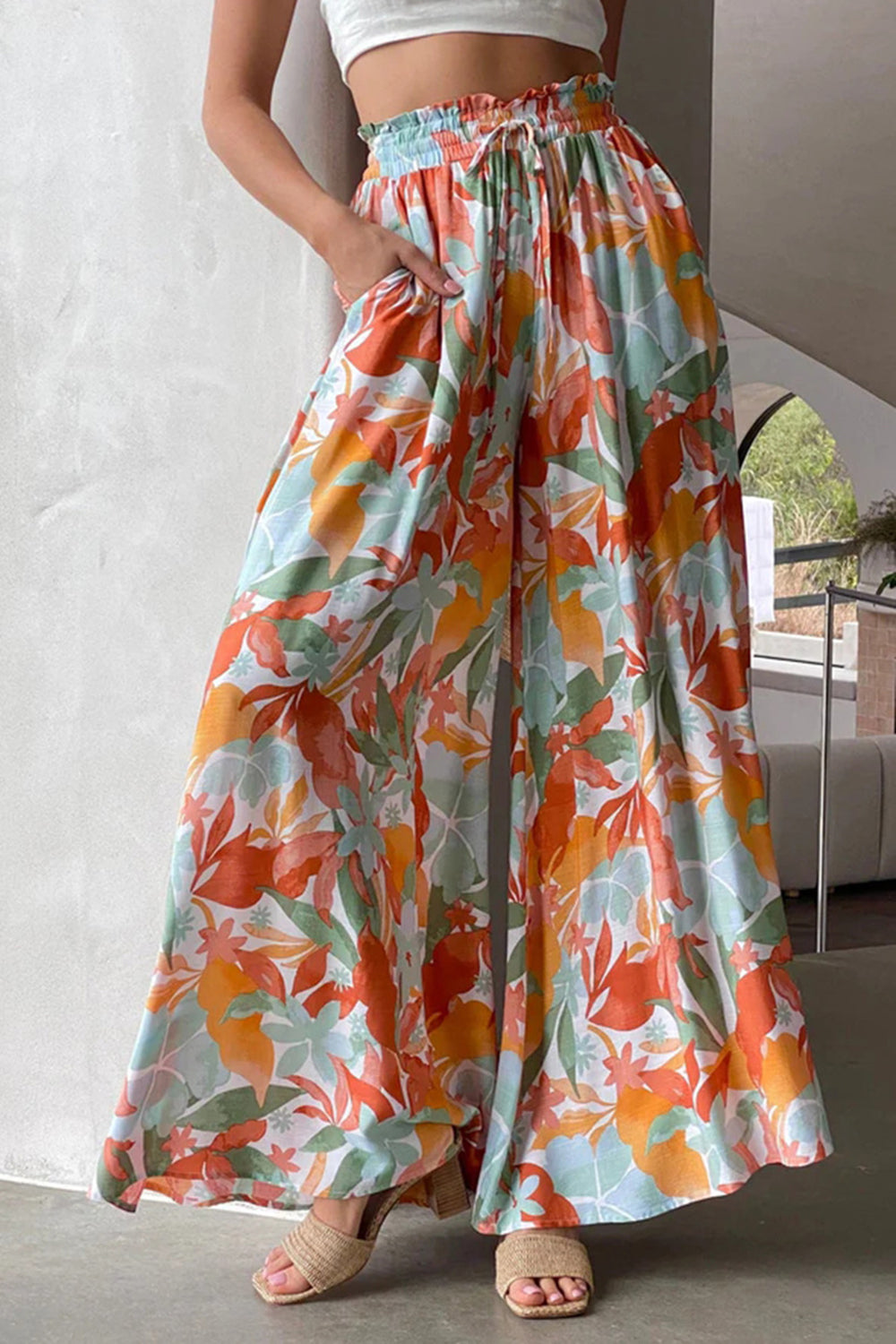 Botanical print palazzo trousers with a drawstring waist and wide legs in orange, aqua, and green.