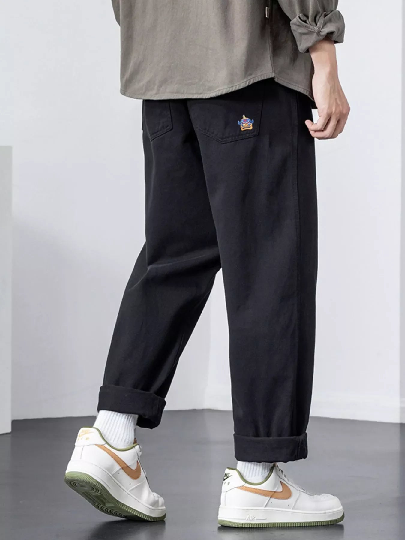 Black cotton wide-leg trousers with cuffed hems and embroidered pocket detail.