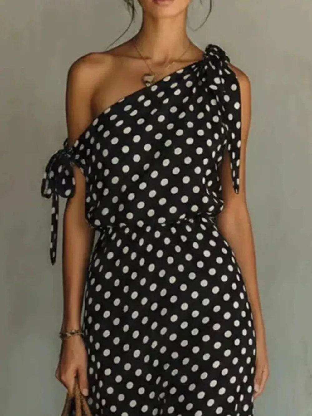 Black polka dot one-shoulder maxi dress with cinched waist and tie details.