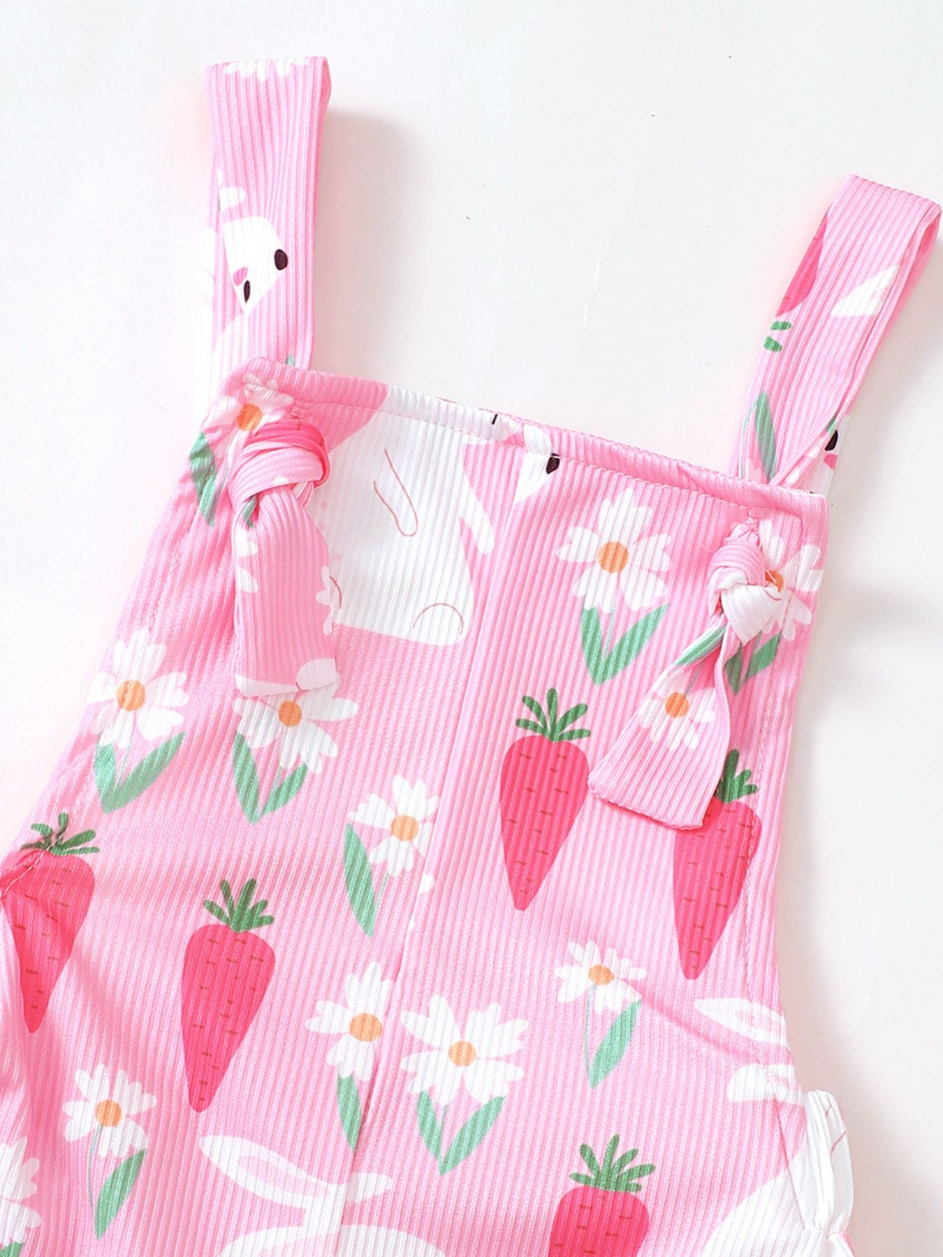 Pink baby overalls with bunny and carrot print, featuring adjustable tie straps.