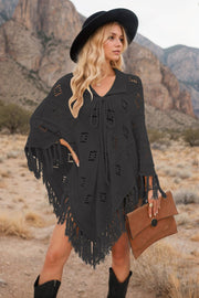 Black knit poncho with geometric cutouts and fringe detail, featuring a tie neckline.
