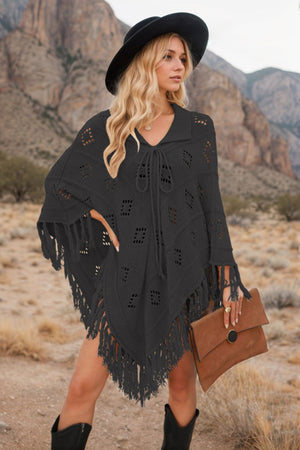 Black knit poncho with geometric cutouts and fringe detail, featuring a tie neckline.