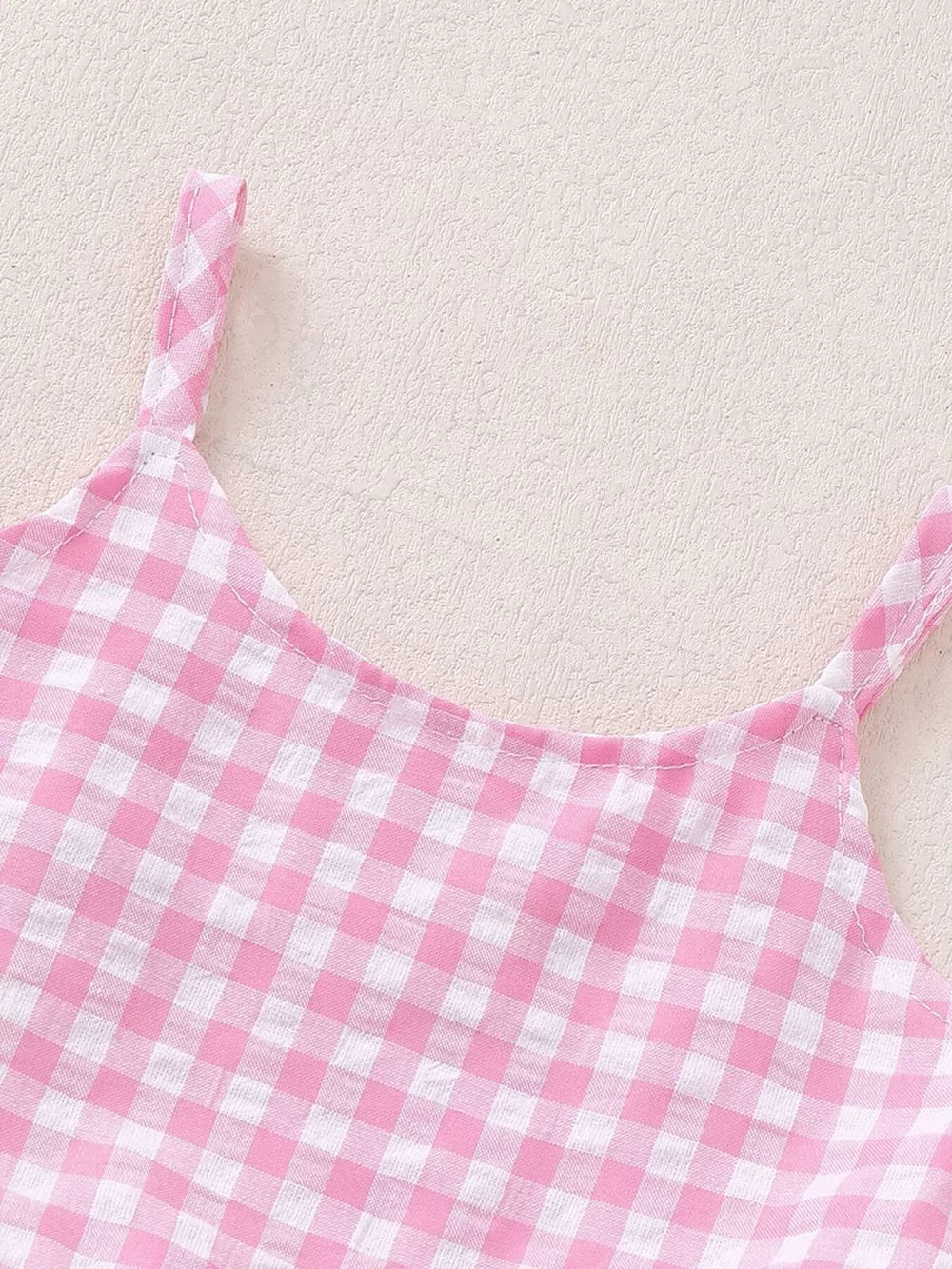Pink gingham ruffled tank top with white straps.