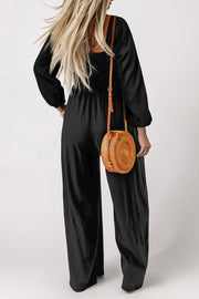 Black smocked bodice wide leg jumpsuit with puff sleeves and a square neckline.