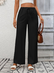 Black high-waist wide-leg pants with drawstring and pockets, styled with slides.