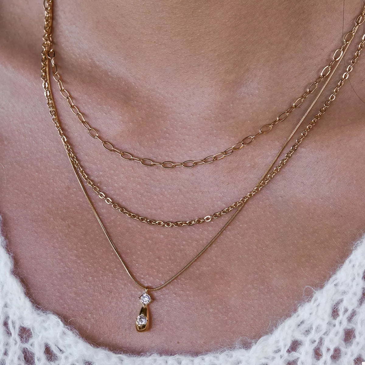 Gold three-layered pendant necklace with two clear stones and a teardrop charm.