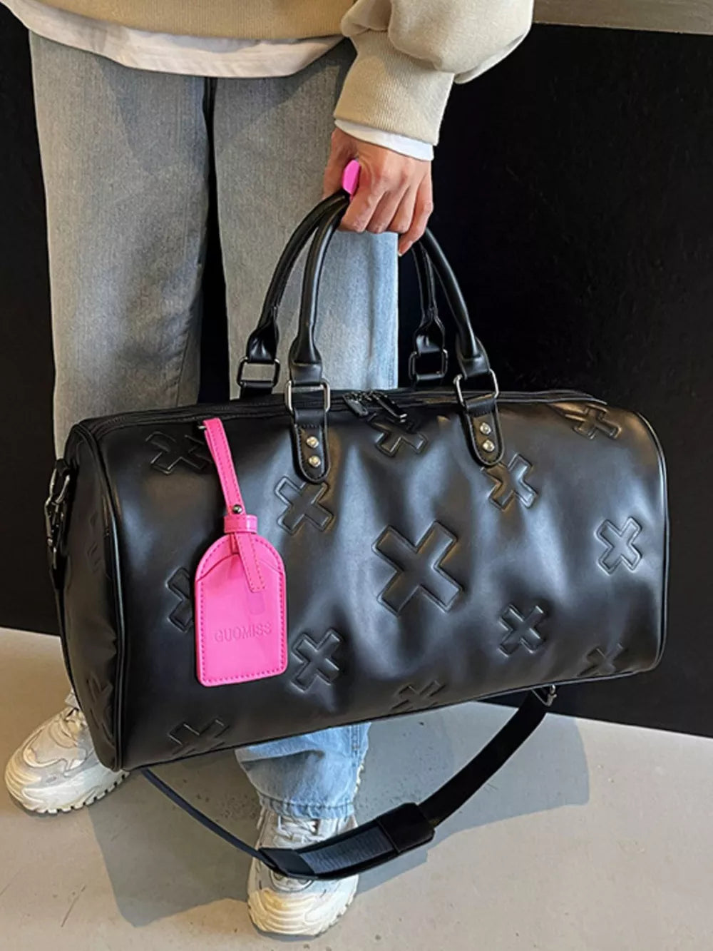 Black embossed cross detail luxury duffel bag with pink tag and strap.