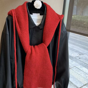Red hooded knit tie scarf with ties, worn over a black jacket.