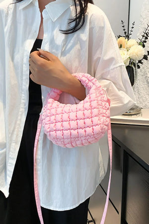 Pink padded crescent crossbody bag with sculptural texture and a long strap.