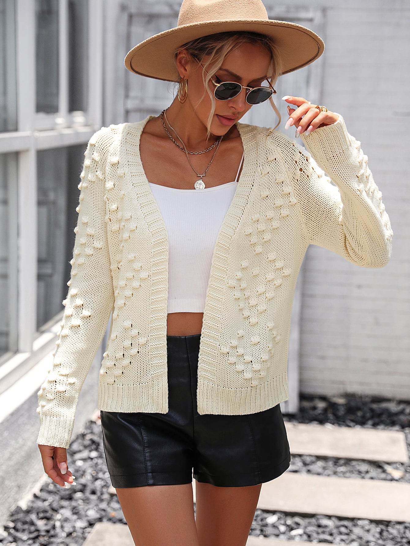 Cream acrylic cardigan with textured bobble details and open front, styled with a white tank and black shorts.