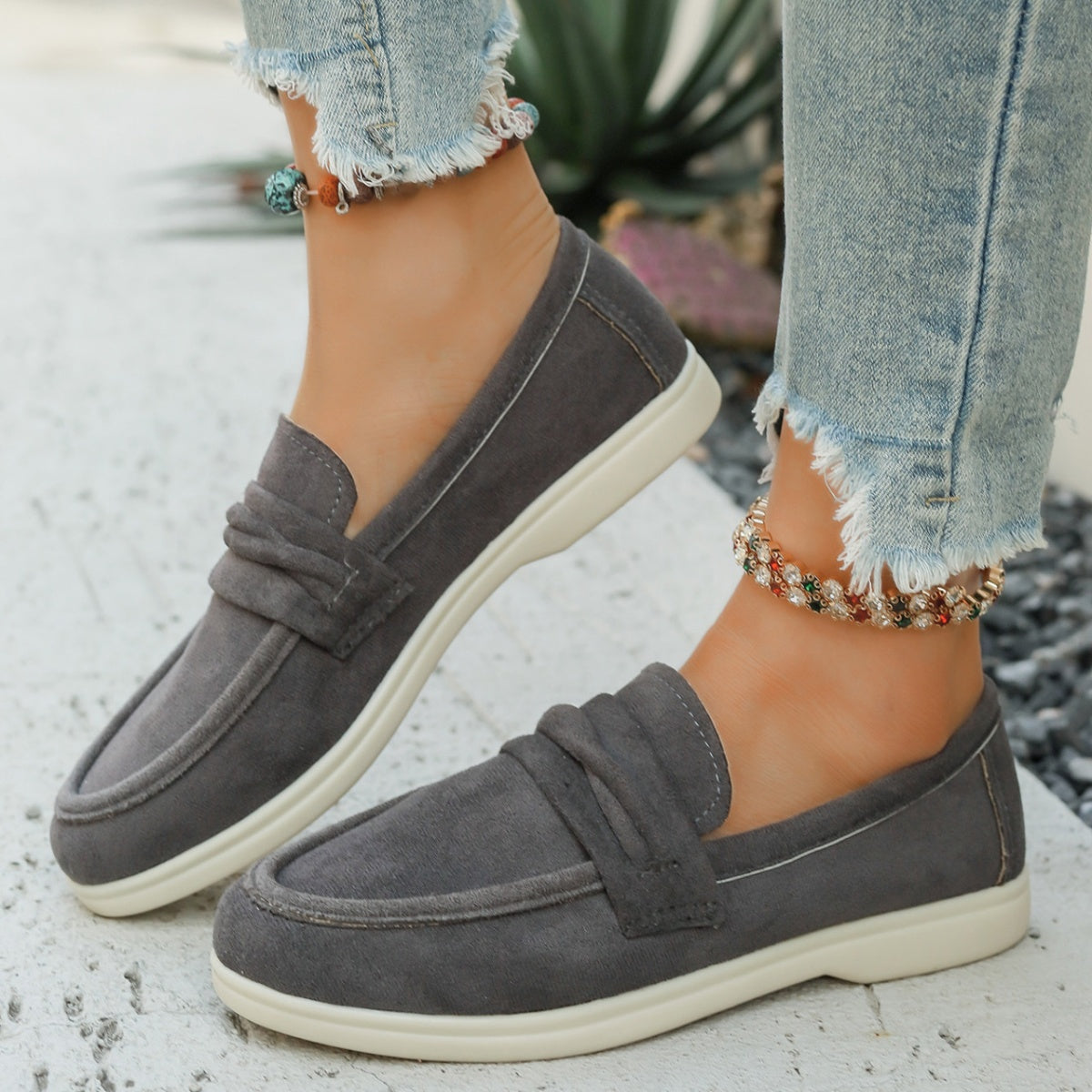 Grey canvas slip-on loafers with a round toe and knotted detail, paired with distressed jeans.