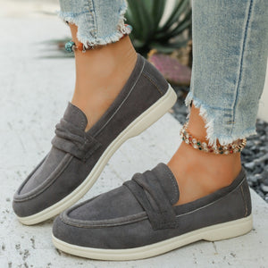 Grey canvas slip-on loafers with a round toe and knotted detail, paired with distressed jeans.
